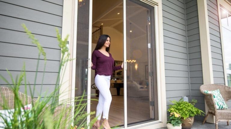 Homeowner effortlessly opening Phantom Screens for French Doors on French doors in Newport Beach, showcasing a seamless blend of style and function.